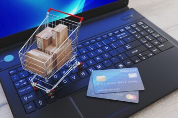 Mini shopping cart with boxes on a laptop keyboard next to a credit card, this content explaned (ecommerce solutions).